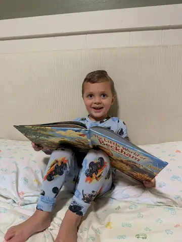 A child smiling while holding an open personalized Sundayfawn hardcover in bed.